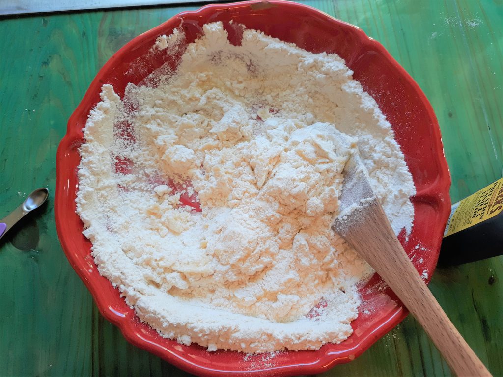 almond raspberry cookie dough before it is mixed in a red bowl with a wooden spoon, on a green wooden table