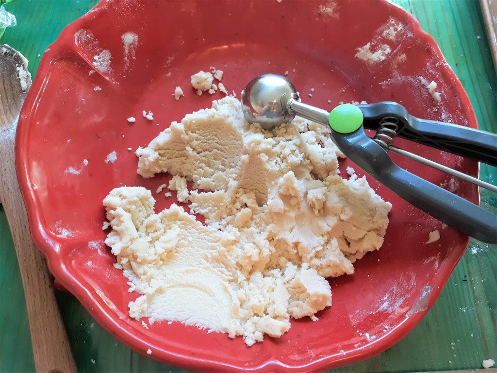 almond raspberry cookie dough in a red bowl with a cookie scoop, on a green wooden table with a wooden spoon