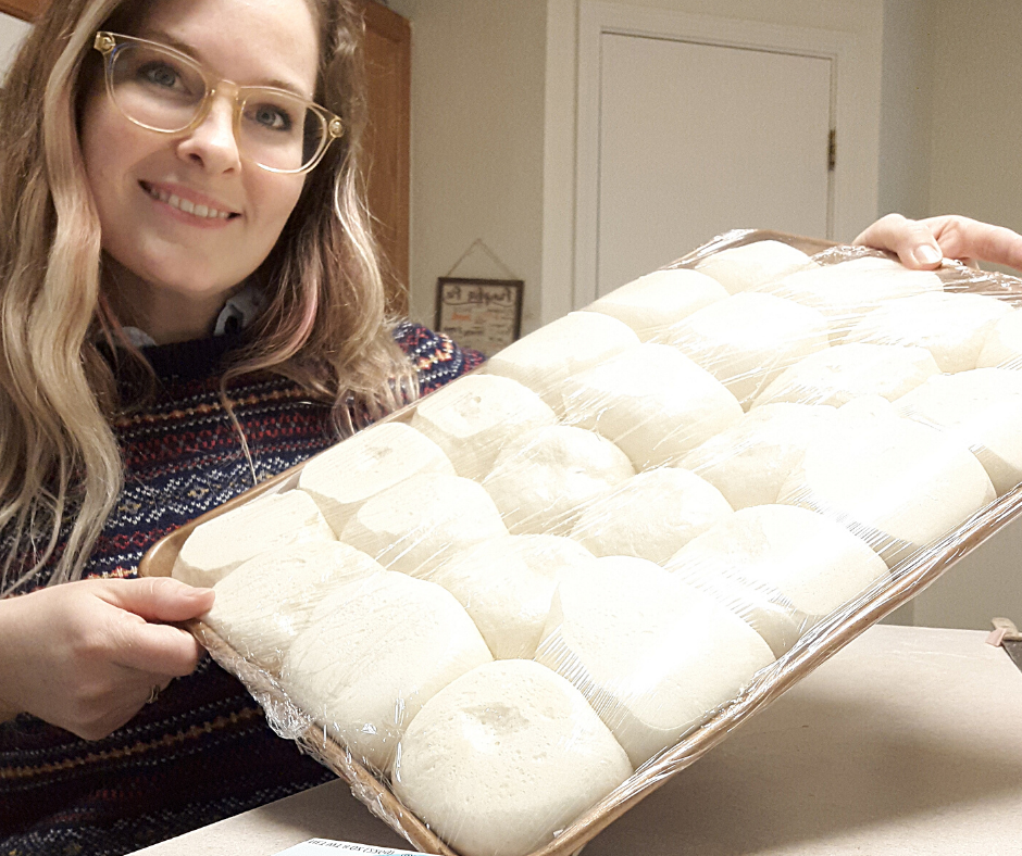 a woman in a sweater holding a pan of risen dough balls