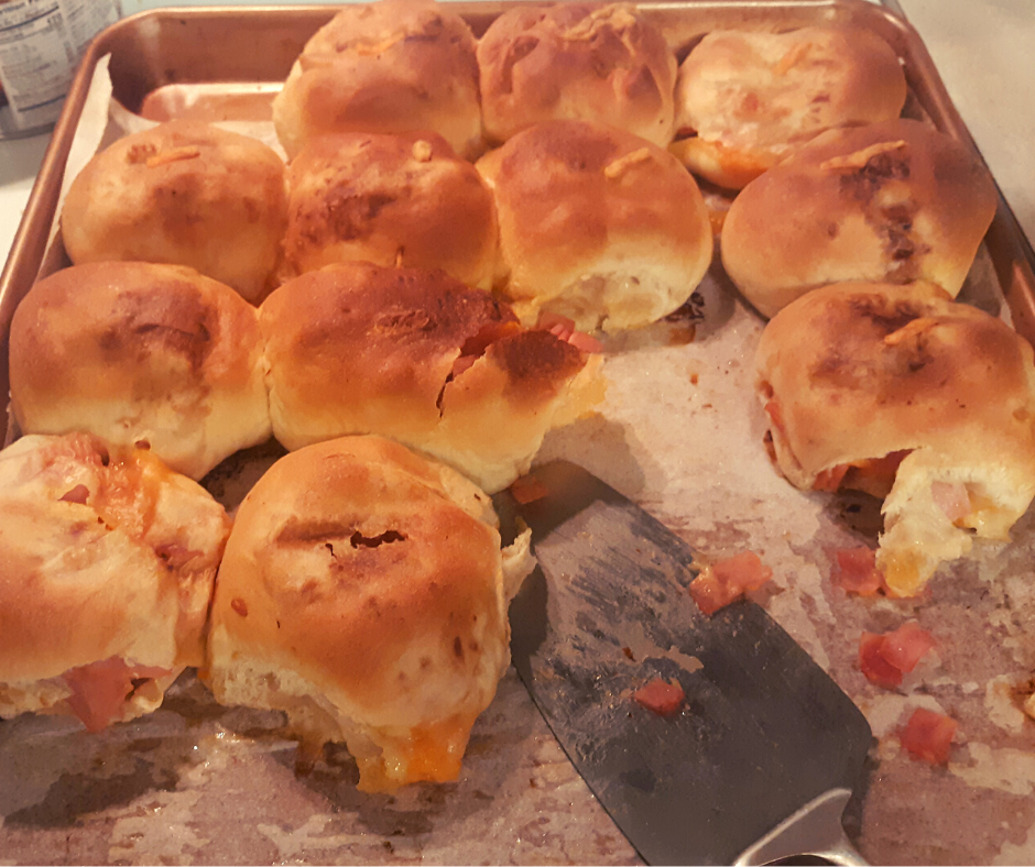 a pan of baked ham and cheese stuffed rolls with several missing and a serving spatula