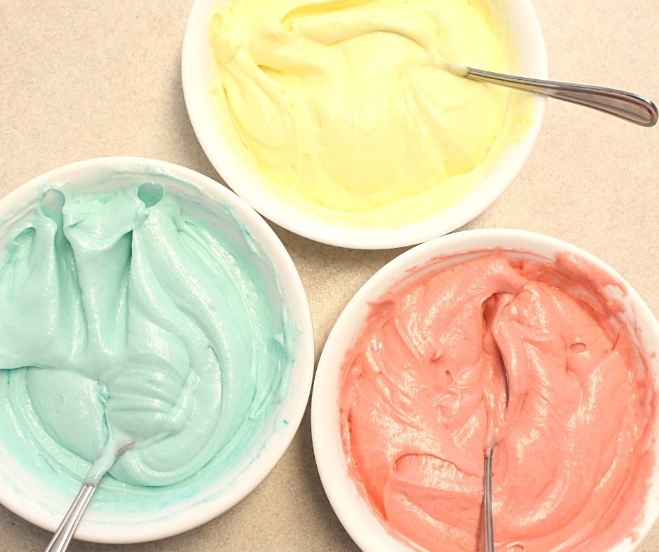 three bowls of yellow, blue, and pink cheesecake frosting