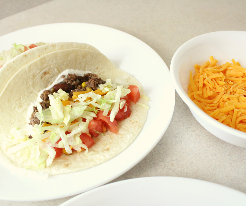 taco meat, shredded cheese, shredded lettuce, diced tomatoes, sour cream on a tortilla