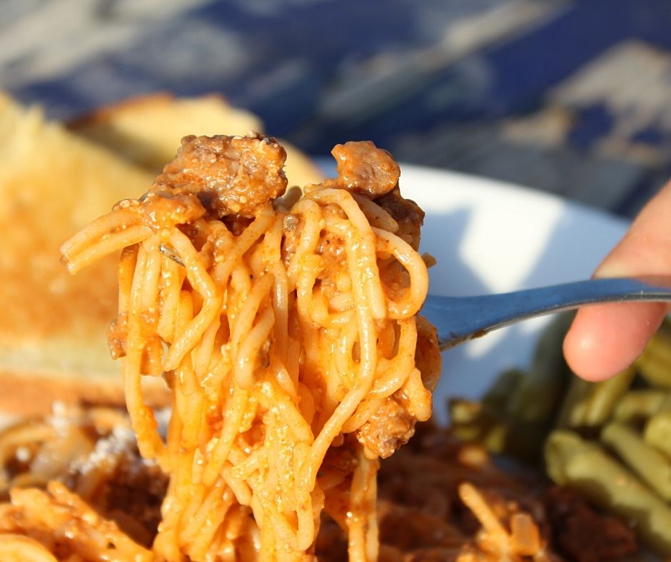 creamy spaghetti on a fork with garlic bread and green beans in the background