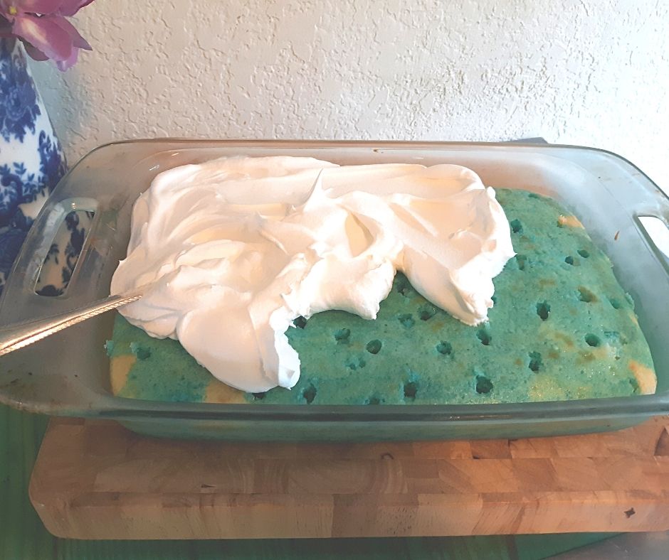 covering the blue poke cake with whipped cream.