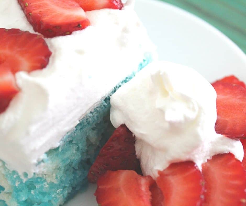 a blue and white poke cake with strawberries and whipped cream on the side.