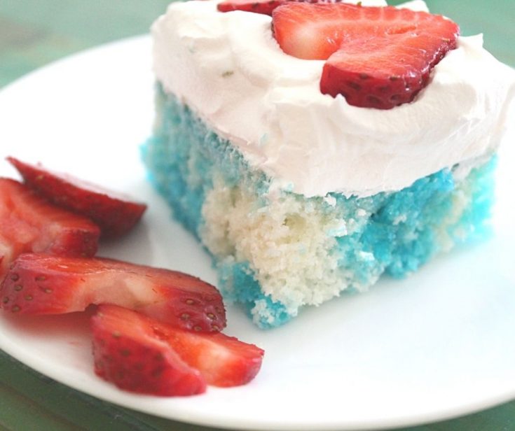 a slice of blue and white poke cake on a white plate with whipped cream and strawberries