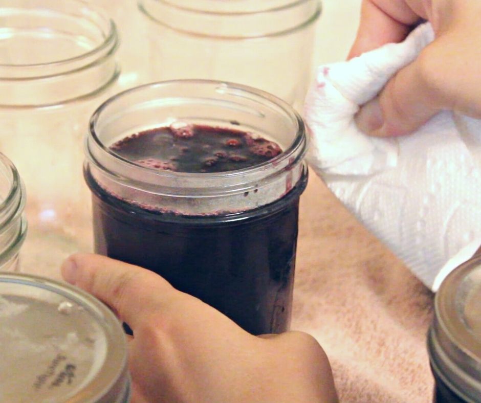 a hand wiping the tops of a mustang grape jelly jar