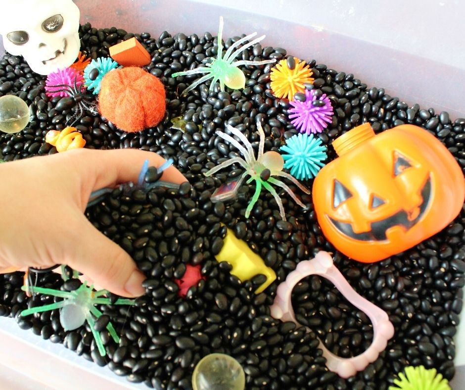 a hand digging in dried black beans and Halloween toys during a Halloween activity