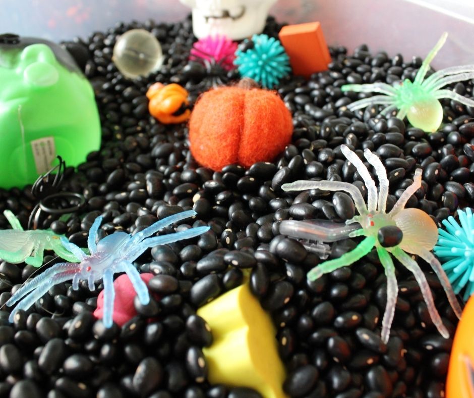 glow in the dark spiders, a pumpkin and other Halloween toys in dried black beans in a Halloween activity