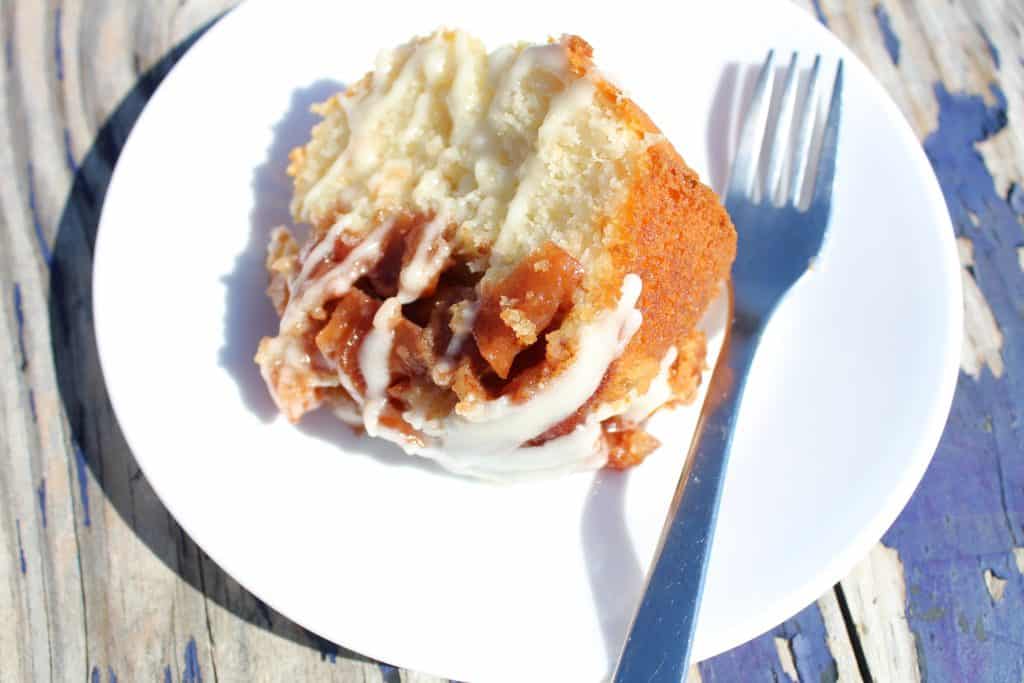 apple pie filling on a white cake on a white plate with white frosting drizzle and a fork.