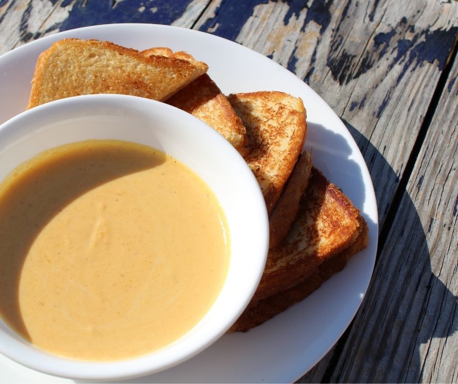 butternut squash soup in a white bowl with grilled cheese triangles