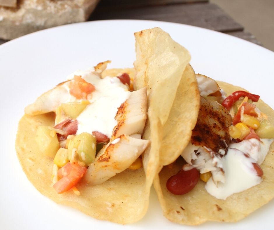 two fish tacos with seasoned fish and sour cream sauce