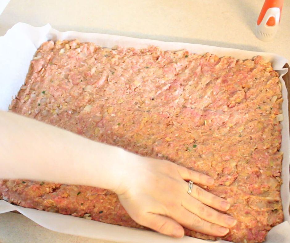 meatloaf mixture being pressed into pan with hand