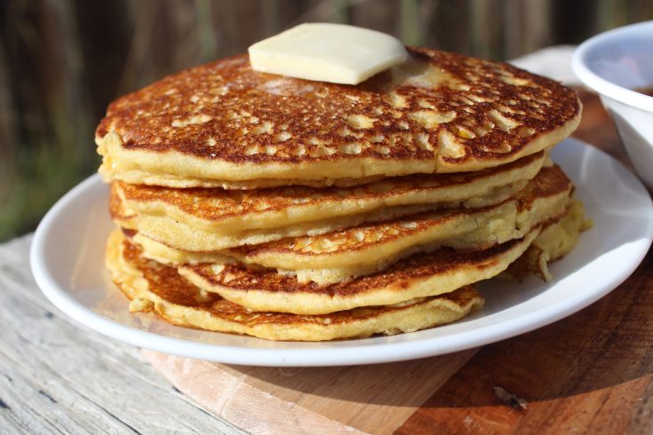 a stack of cornbread pancakes with butter on top on a white plate