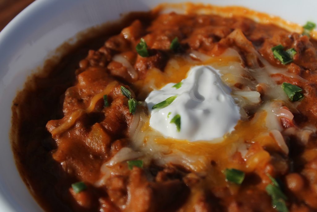close up of chili with cheese, sour cream, and chives