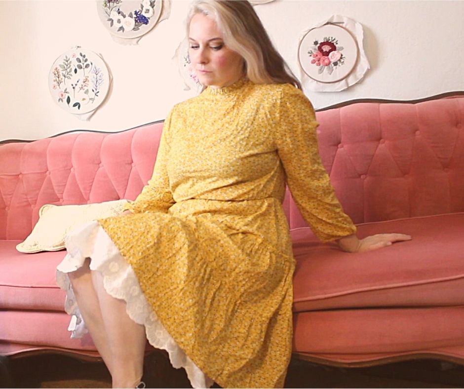 girl wearing a yellow dress with a white lace underskirt, sitting on a pink couch