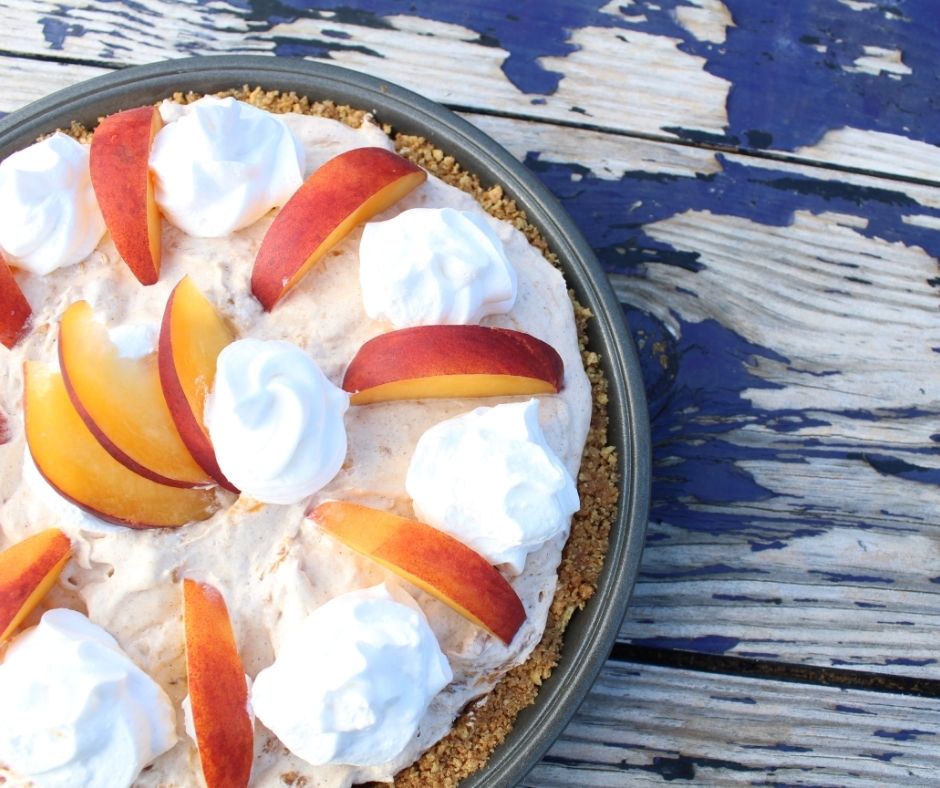 whipped peach pie with whipped cream and slices of peaches on top, on a wooden table with peeling blue paint