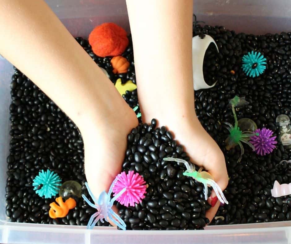 hands scooping a handful of dried black beans and Halloween toys for a Halloween Activity