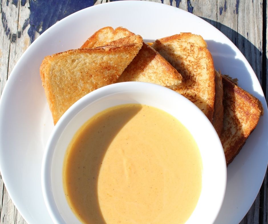 butternut squash soup in a white bowl with grilled cheese triangles